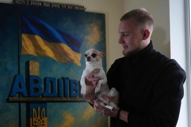 Kostiantyn Kosik, a 18-year-old displaced person from Avdiivka in Donetsk region, poses holding a puppy in his own room in Irpin, on October 20, 2025. It's not so simple for Kostiantyn Kosik, who is on medication for his tics, faintness and migraines. "I'm constantly nervous, on edge. It's because of the war. It has a huge effect on my health," said the bearded 18-year-old, who was dressed in black. (Photo by OLEKSII FILIPPOV / AFP)