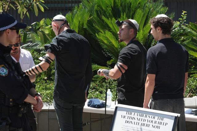 Mourners wearing their tefillin arrive for the funeral of rabbi Eli Schlanger, who was killed in the December 14 Bondi beach shooting attack, at the Chabad of Bondi Synagogue in Sydney on December 17, 2025. Australia held the first funeral on December 17 for victims of the Bondi Beach mass shooting, as large crowds gathered to grieve a rabbi slain in the attack. Sajid Akram and his son Naveed opened fire on a Jewish festival at the famed surf beach on December 14 evening, killing 15 people and wounding dozens more. (Photo by DAVID GRAY / AFP)