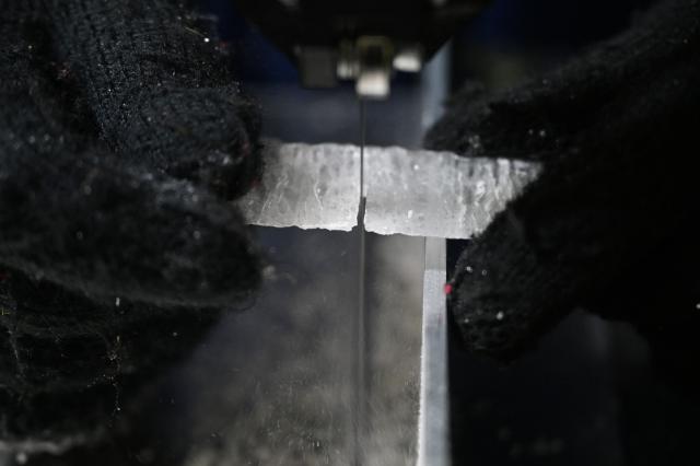 A researcher cuts a slice from an ice core sample taken from a glacier in the Pamir mountain range in Tajikistan, at the Hokkaido University Institute of Low Temperature Science, in Sapporo, in northern Japan’s Hokkaido prefecture on December 9, 2025. Dressed in an orange puffer jacket, Japanese glacier scientist Yoshinori Iizuka stepped into a storage freezer chilled to minus 50 Celcius to retrieve an ice core. (Photo by GREG BAKER / AFP) / TO GO WITH: Japan-Tajikistan-climate-science-environment-research, FOCUS by Hiroshi HIYAMA