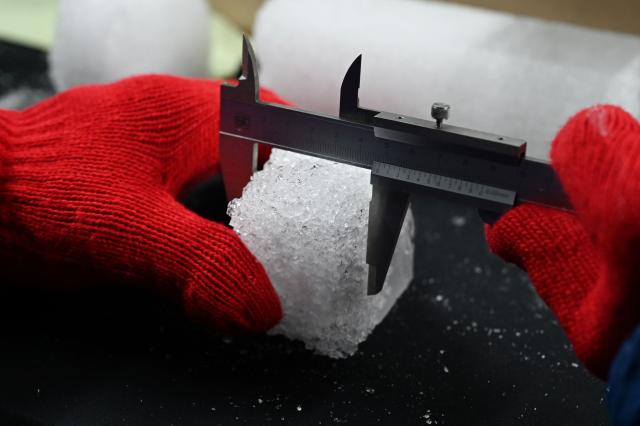 A researcher measures a piece of an ice core sample taken from a glacier in the Pamir mountain range in Tajikistan, at the Hokkaido University Institute of Low Temperature Science, in Sapporo, in northern Japan’s Hokkaido prefecture on December 9, 2025. Dressed in an orange puffer jacket, Japanese glacier scientist Yoshinori Iizuka stepped into a storage freezer chilled to minus 50 Celcius to retrieve an ice core. (Photo by GREG BAKER / AFP) / TO GO WITH: Japan-Tajikistan-climate-science-environment-research, FOCUS by Hiroshi HIYAMA
