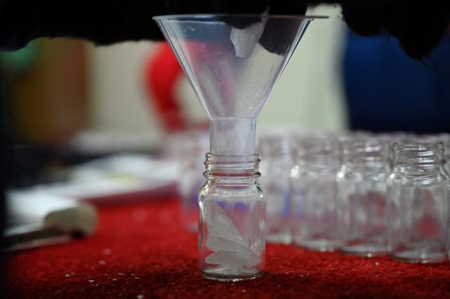 A researcher drops slices of ice from an ice core sample taken from a glacier in the Pamir mountain range in Tajikistan into a bottle at the Hokkaido University Institute of Low Temperature Science, in Sapporo, in northern Japans Hokkaido prefecture on December 9, 2025. Dressed in an orange puffer jacket, Japanese glacier scientist Yoshinori Iizuka stepped into a storage freezer chilled to minus 50 Celcius to retrieve an ice core. (Photo by GREG BAKER / AFP) / TO GO WITH: Japan-Tajikistan-climate-science-environment-research, FOCUS by Hiroshi HIYAMA