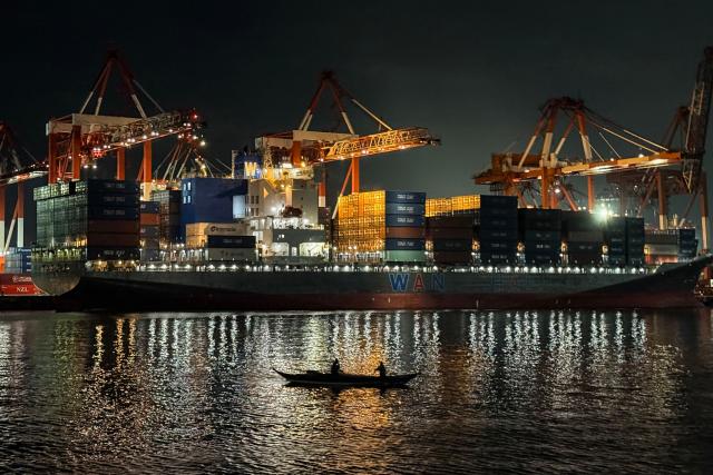 Fishermen paddle past a cargo ship unloading containers at the Manila international port in Manila on December 16, 2025. (Photo by Ted ALJIBE / AFP)