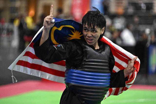 Malaysia’s Ummi Mashitah Hassan holds the Malaysian flag after winning the women's individual Pencat Silat final during the 33rd Southeast Asian Games (SEA Games) at IMPACT Arena in Nonthaburi on December 17, 2025. (Photo by Lillian SUWANRUMPHA / AFP)