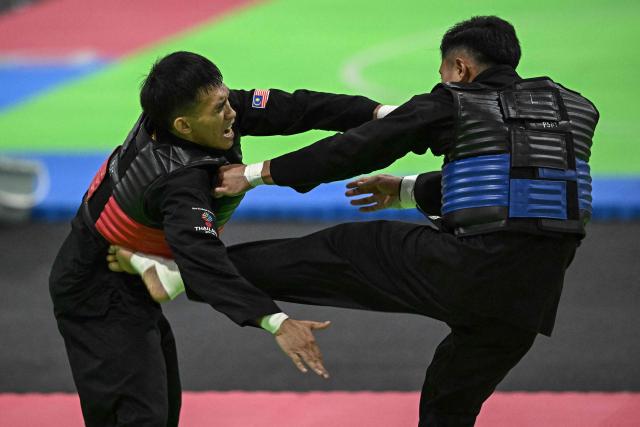 Thailand’s Peerapon Mitasarn (R) competes against Malaysia’s Muhammad Izzul Irfan Marzuki (L) in the men’s individual Pencat Silat final during the 33rd Southeast Asian Games (SEA Games) at IMPACT Arena in Nonthaburi on December 17, 2025. (Photo by Lillian SUWANRUMPHA / AFP)