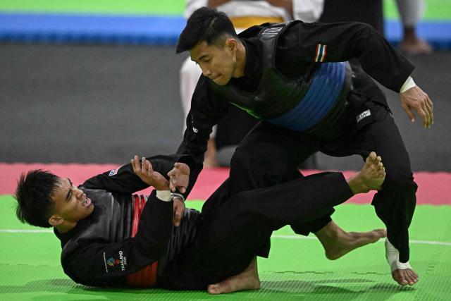 Thailand’s Peerapon Mitasarn (R) competes against Malaysia’s Muhammad Izzul Irfan Marzuki (L) in the men’s individual Pencat Silat final during the 33rd Southeast Asian Games (SEA Games) at IMPACT Arena in Nonthaburi on December 17, 2025. (Photo by Lillian SUWANRUMPHA / AFP)