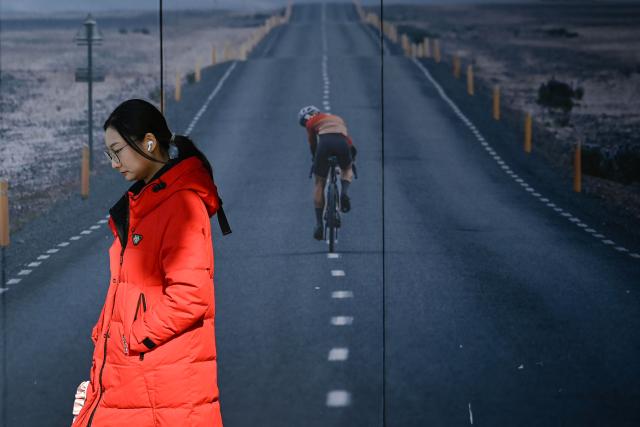 A woman walks past a poster outside a store in Beijing on December 17, 2025. (Photo by WANG Zhao / AFP)
