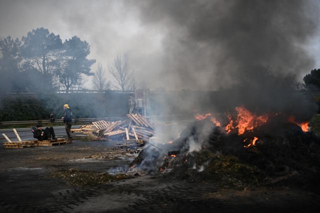French farmers union Coordination Rurale members sit by a bonfire at their blockade of the A63 motorway at the Cestas interchange in Gironde, south-western France, on December 17, 2025. French farmers have been protesting against the government's mandatory culling protocol for cattle herds affected by lumpy skin disease (dermatose nodulaire contagieuse), a viral disease first detected in France in June 2025 that has led to the slaughter of over 3,000 cattle across more than 110 outbreaks nationwide. (Photo by Christophe ARCHAMBAULT / AFP)