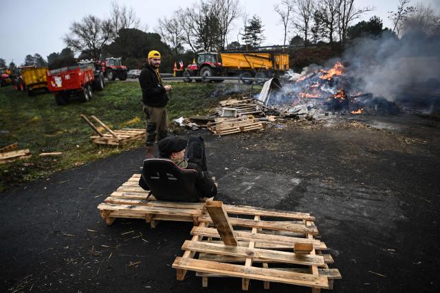French farmers union Coordination Rurale members sit by a bonfire at their blockade of the A63 motorway at the Cestas interchange in Gironde, south-western France, on December 17, 2025. French farmers have been protesting against the government's mandatory culling protocol for cattle herds affected by lumpy skin disease (dermatose nodulaire contagieuse), a viral disease first detected in France in June 2025 that has led to the slaughter of over 3,000 cattle across more than 110 outbreaks nationwide. (Photo by Christophe ARCHAMBAULT / AFP)