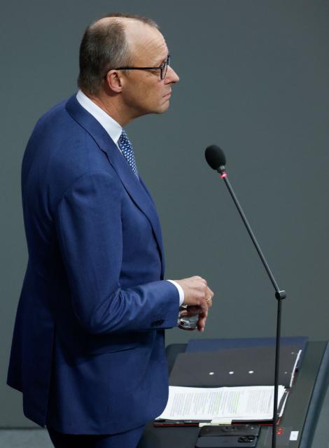 German Chancellor Friedrich Merz stands at a microphone as he listens to questions from parliamentarians to the government during a question time at the Bundestag (lower house of parliament) in Berlin, on December 17, 2025. (Photo by Odd ANDERSEN / AFP)