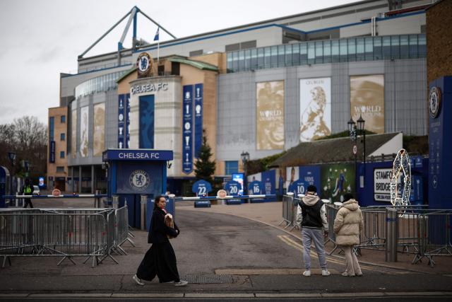 People walk outside the grounds of Stamford Bridge, the home of English Premier League team Chelsea, formally owned by Russian businessman Roman Abramovich, in London on December 17, 2025. Britain's Prime Minister Keir Starmer on December 17, 2025 warned former Chelsea owner Roman Abramovich "the clock is ticking" over the frozen £2.5 billion (3.4 billion USD) generated from the sale of the club, which has been earmarked to help Ukraine's war victims. A consortium led by US businessman Todd Boehly bought the Premier League giants after Abramovich was sanctioned following Russian President Vladimir Putin's invasion of Ukraine. (Photo by HENRY NICHOLLS / AFP)