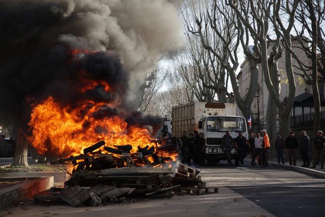 This photograph shows a fire as farmers and members of agricultural unions gather in front of the Aude prefecture, in Carcassonne, south-western France, on December 17, 2025, as part of a nationwide action by farmers to protest against the government's mandatory culling protocol for cattle herds affected by lumpy skin disease (dermatose nodulaire contagieuse). The viral disease first detected in France in June 2025 that has led to the slaughter of over 3,000 cattle across more than 110 outbreaks nationwide. (Photo by Valentine CHAPUIS / AFP)