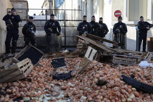 French Republican Security Corps (CRS - Compagnies Republicaines de Securite) police officers stand as farmers and members of various agricultural unions gather in front of the Aude prefecture, in Carcassonne, south-western France, on December 17, 2025, as part of a nationwide action by farmers to protest against the government's mandatory culling protocol for cattle herds affected by lumpy skin disease (dermatose nodulaire contagieuse). The viral disease first detected in France in June 2025 that has led to the slaughter of over 3,000 cattle across more than 110 outbreaks nationwide. (Photo by Valentine CHAPUIS / AFP)