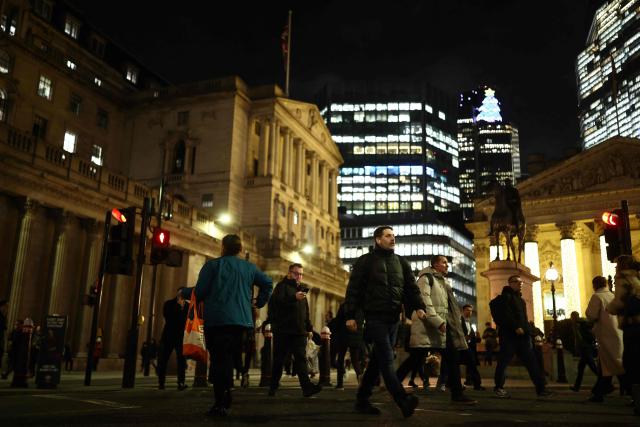 Pedestrians walk by the Bank of England building (L) and The Royal Exchange (R) in the City of London on December 17, 2025. Britain's annual inflation rate slowed more than expected in November to 3.2 percent, official data showed December 17, cementing expectations that the Bank of England will cut its main interest rate on December 18. (Photo by Henry NICHOLLS / AFP)