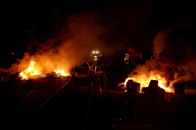 Protesters light burning barricades as they block the A61 motorway near Carcassonne as part of a nationwide action by farmers to protest against the government's mandatory culling protocol for cattle herds affected by lumpy skin disease (dermatose nodulaire contagieuse), in Carcassonne, southern France, on December 17, 2025. The viral disease first detected in France in June 2025 that has led to the slaughter of over 3,000 cattle across more than 110 outbreaks nationwide. (Photo by Valentine CHAPUIS / AFP)
