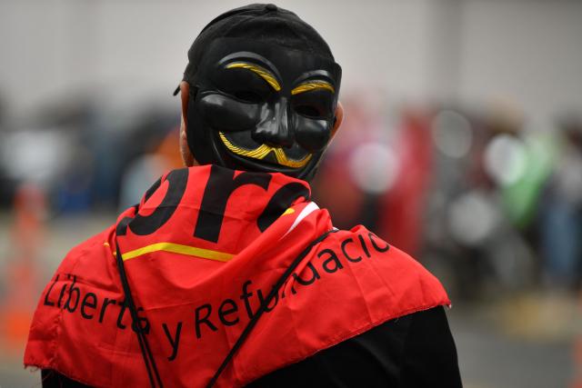 A supporter of the ruling Libertad y Refundacion (LIBRE) party wearing a black Guy Fawkes mask stands in front of the Presidential House in support of Honduran President Xiomara Castro in Tegucigalpa on December 17, 2025. (Photo by Orlando SIERRA / AFP)