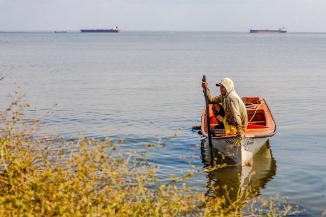 A man looks on at a boat with two crude oil tankers in the background on Lake Maracaibo, near Maracaibo, Zulia state, Venezuela on December 17, 2025. (Photo by Alejandro Paredes / AFP)