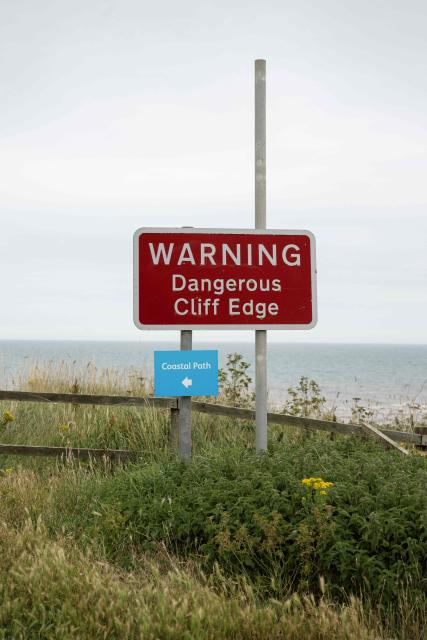 A photograph taken on June 17, 2025 shows a sign warning of dangerous cliffs and the direction of a clifftop coastal path on a section of the North Sea coast that is undergoing coastal erosion, near the village of Barmston, near Bridlington, in the East Riding of Yorkshire, north eastern England. The Holderness coastline, covering 61km between the Spurn nature reserve in the south and Flamborough in the north, experiences one of the fastest rates of erosion in Europe. The Holderness cliffs are eroding at average rate of around 1.5 metres per year, although individual cliff losses can exceed 20 metres per year. Over the last 1000 years, the coast has retreated by around 2 kilometres, resulting in the destruction of 26 villages listed in the Domesday survey of 1086. (Photo by Oli SCARFF / AFP)