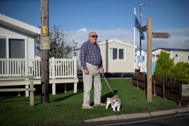 Richard Armstrong stands with his dog Mille outside Barmston Beach Holiday Park, where he has a caravan, located on the North sea coast in an area which is experiencing intense coastal erosion, near Bridlington, in the East Riding of Yorkshire, north eastern England, on November 13, 2025. The Holderness coastline, covering 61km between the Spurn nature reserve in the south and Flamborough in the north, experiences one of the fastest rates of erosion in Europe. The Holderness cliffs are eroding at average rate of around 1.5 metres per year, although individual cliff losses can exceed 20 metres per year. Over the last 1000 years, the coast has retreated by around 2 kilometres, resulting in the destruction of 26 villages listed in the Domesday survey of 1086. (Photo by Oli SCARFF / AFP)