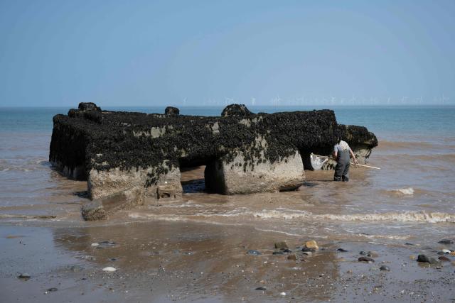 A man fishes for bait around the remnants of the Godwin Artillery Battery, initially constructed on the cliff top in 1915, but now located on the beach following intense coastal erosion, near the village of Kilnsea, near Withernsea, in the East Riding of Yorkshire, north eastern England, on June 17, 2025. The Holderness coastline, covering 61km between the Spurn nature reserve in the south and Flamborough in the north, experiences one of the fastest rates of erosion in Europe. The Holderness cliffs are eroding at average rate of around 1.5 metres per year, although individual cliff losses can exceed 20 metres per year. Over the last 1000 years, the coast has retreated by around 2 kilometres, resulting in the destruction of 26 villages listed in the Domesday survey of 1086. (Photo by Oli SCARFF / AFP)