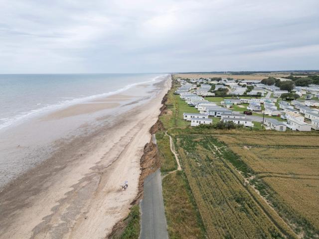 An aerial photograph taken on July 17, 2025 shows a view of a collapsed road and clifftop static caravan park on the North Sea coast that is undergoing coastal erosion, near the village of Skipsea, near Bridlington, in the East Riding of Yorkshire, north eastern England. The Holderness coastline, covering 61km between the Spurn nature reserve in the south and Flamborough in the north, experiences one of the fastest rates of erosion in Europe. The Holderness cliffs are eroding at average rate of around 1.5 metres per year, although individual cliff losses can exceed 20 metres per year. Over the last 1000 years, the coast has retreated by around 2 kilometres, resulting in the destruction of 26 villages listed in the Domesday survey of 1086. (Photo by Oli SCARFF / AFP)