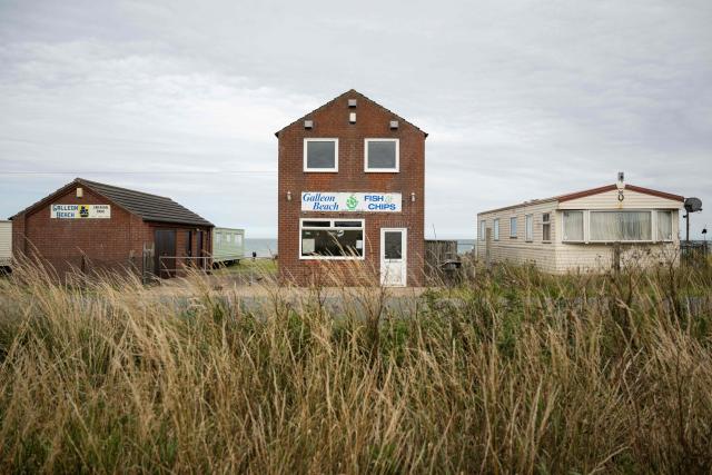 A photograph taken on July 17, 2025 shows a former fish and chips shop next to a static caravan park on the North Sea coast that is undergoing coastal erosion, near the village of Skipsea, near Bridlington, in the East Riding of Yorkshire, north eastern England. The Holderness coastline, covering 61km between the Spurn nature reserve in the south and Flamborough in the north, experiences one of the fastest rates of erosion in Europe. The Holderness cliffs are eroding at average rate of around 1.5 metres per year, although individual cliff losses can exceed 20 metres per year. Over the last 1000 years, the coast has retreated by around 2 kilometres, resulting in the destruction of 26 villages listed in the Domesday survey of 1086. (Photo by Oli SCARFF / AFP)