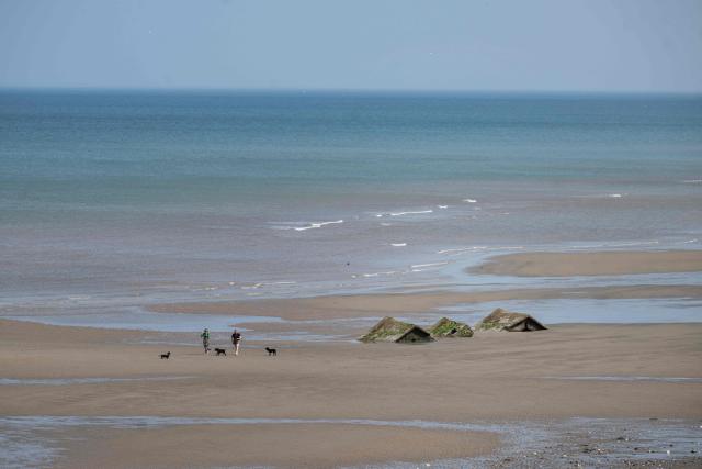 People walk past remnants of World War military defences, formerly located on the cliff top, now lying on the beach due to intense coastal erosion, near the village of Great Cowden, near Hornsea, in the East Riding of Yorkshire, north eastern England, on June 17, 2025. The Holderness coastline, covering 61km between the Spurn nature reserve in the south and Flamborough in the north, experiences one of the fastest rates of erosion in Europe. The Holderness cliffs are eroding at average rate of around 1.5 metres per year, although individual cliff losses can exceed 20 metres per year. Over the last 1000 years, the coast has retreated by around 2 kilometres, resulting in the destruction of 26 villages listed in the Domesday survey of 1086. (Photo by Oli SCARFF / AFP)