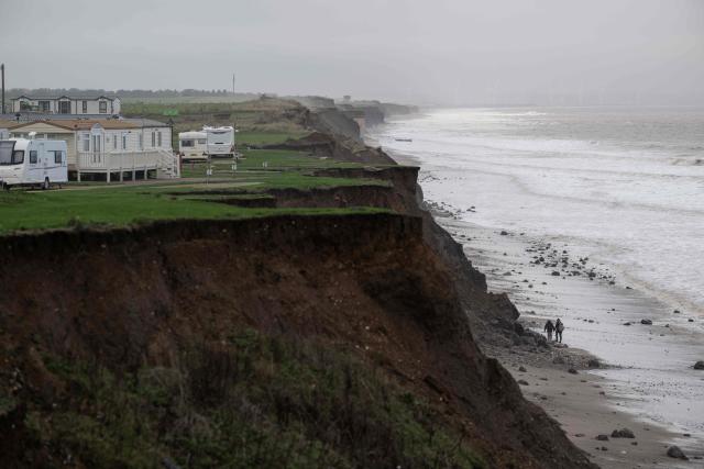 Two men with geological hammers walk along the beach beneath Cliff Top Caravan Park, near the village of Atwick, on the North sea coast in an area which is experiencing intense coastal erosion, near Bridlington, in the East Riding of Yorkshire, north eastern England, on November 13, 2025. The Holderness coastline, covering 61km between the Spurn nature reserve in the south and Flamborough in the north, experiences one of the fastest rates of erosion in Europe. The Holderness cliffs are eroding at average rate of around 1.5 metres per year, although individual cliff losses can exceed 20 metres per year. Over the last 1000 years, the coast has retreated by around 2 kilometres, resulting in the destruction of 26 villages listed in the Domesday survey of 1086. (Photo by Oli SCARFF / AFP)