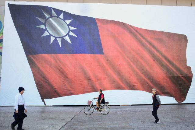 (FILES) People walk past a Taiwan flag in New Taipei City on January 13, 2024. Donald Trump's administration has given its approval to sell $11 billion of weapons to Taiwan, the second batch of such sales since the US president returned to office, Taipei said on December 18, 2025. (Photo by Sam Yeh / AFP)
