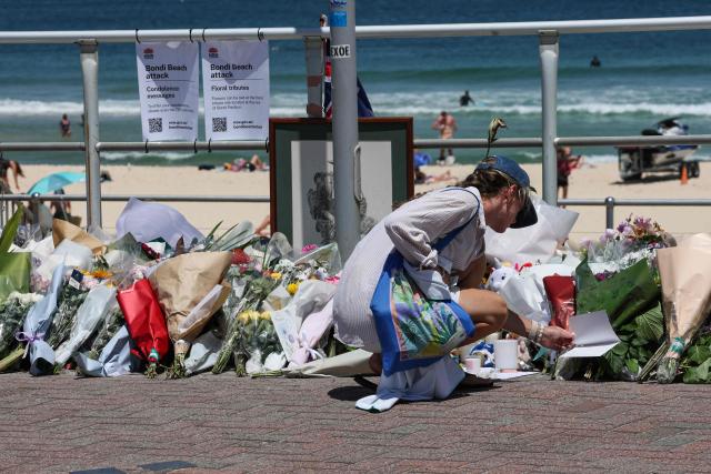 A woman reads a message left near floral tributes at the promenade of Bondi Beach in Sydney on December 18, 2025, to honour victims of the shooting that took place there on December 14. The attack at Bondi Beach on December 14 was one of the deadliest in Australian history. (Photo by DAVID GRAY / AFP)