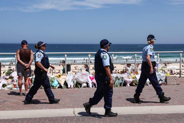 The Police walk past floral tributes left at the promenade of Bondi Beach in Sydney on December 18, 2025, to honour victims of the shooting that took place there on December 14. The attack at Bondi Beach on December 14 was one of the deadliest in Australian history. (Photo by DAVID GRAY / AFP)