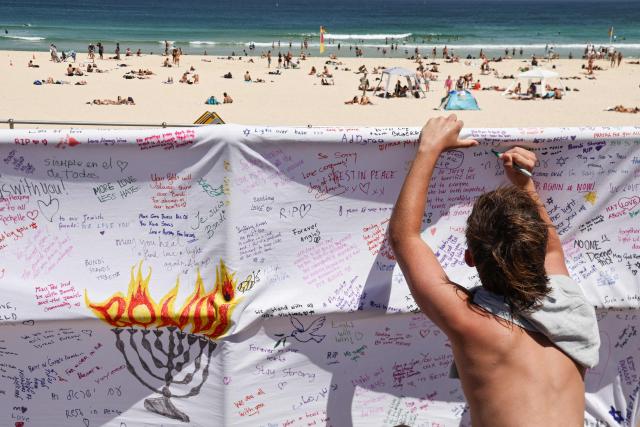 A mourner writes a message of a piece of cloth at the promenade of Bondi Beach in Sydney on December 18, 2025, to honour victims of the shooting that took place there on December 14. The attack at Bondi Beach on December 14 was one of the deadliest in Australian history. (Photo by DAVID GRAY / AFP)