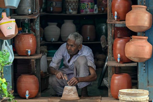 An artisan marks a water drainage hole in a clay plant pot for a customer at his shop during early hours in Mumbai on December 18, 2025. (Photo by Indranil MUKHERJEE / AFP)