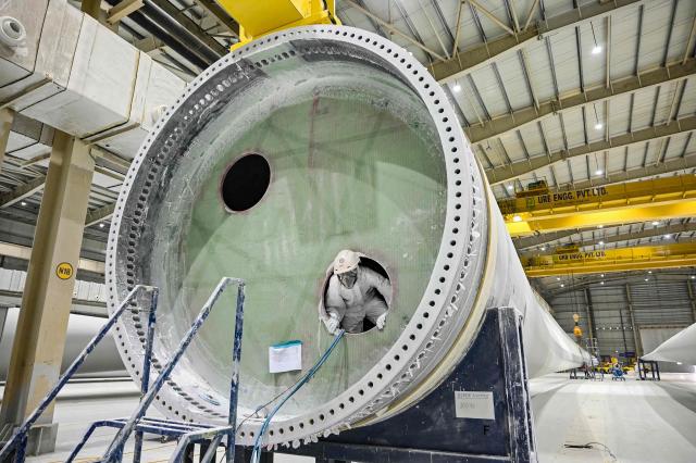 This photograph taken on November 5, 2025 shows an employee in personal protective equipment (PPE) suit working on a wind turbine blade at an Adani Group factory in Gujarat's port city of Mundra. (Photo by Shammi MEHRA / AFP)