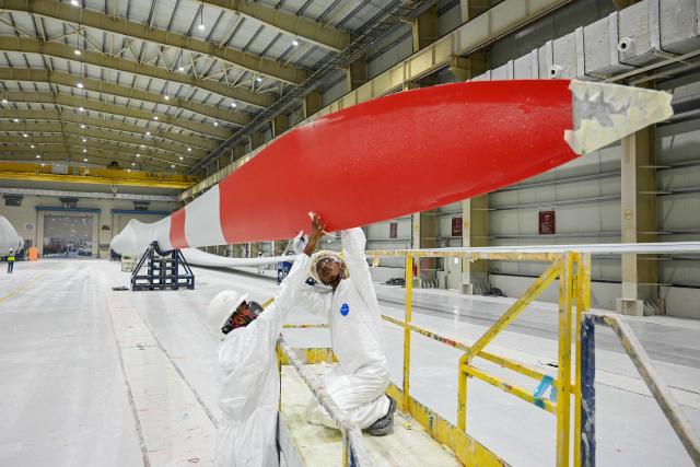 This photograph taken on November 5, 2025 shows employees in personal protective equipment (PPE) suits working on a wind turbine blade at an Adani Group factory in Gujarat's port city of Mundra. (Photo by Shammi MEHRA / AFP)