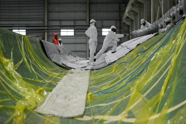 This photograph taken on November 5, 2025 shows employees in personal protective equipment (PPE) suits working on a wind turbine blade at an Adani Group factory in Gujarat's port city of Mundra. (Photo by Shammi MEHRA / AFP)