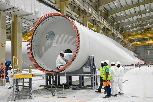 This photograph taken on November 5, 2025 shows employees working on a wind turbine blade at an Adani Group factory in Gujarat's port city of Mundra. (Photo by Shammi MEHRA / AFP)
