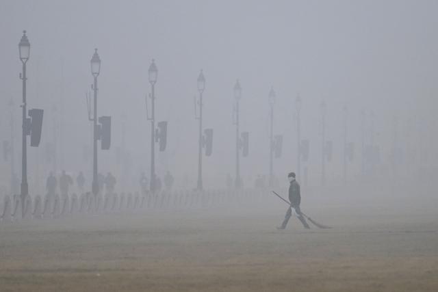 A civic worker covering his face walks along the Kartavya Path amid heavy smog in New Delhi on December 18, 2025. (Photo by Arun SANKAR / AFP)