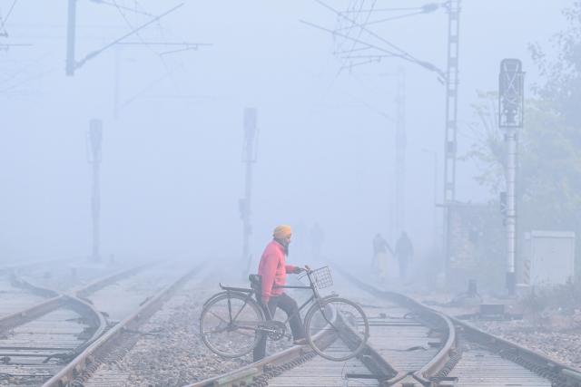A man carrying his bicycle crosses railway tracks amid dense smog on the outskirts of Amritsar on December 18, 2025. (Photo by Narinder NANU / AFP)
