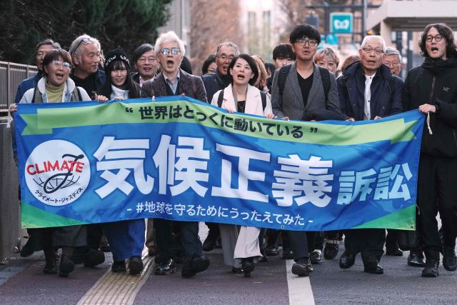 Plaintiffs and their lawyers walk along the sidewalk in front of the Tokyo District Court to appeal that they have filed a lawsuit against the government seeking damages for the government's failure to take action on climate change in Tokyo on December 18, 2025. Hundreds of people across Japan sued the central government on December 18 seeking damages for "unconstitutional" inaction on climate change, the country's first such litigation. (Photo by Kazuhiro NOGI / AFP)