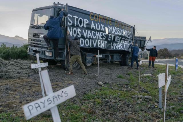 Protestors put up a banner that reads "Citizens' committee: Stop the massacres! Our cows and our farmers must live!" on a roundabout during a farmers' demonstration in Le Boulou, southwestern France, on December 18, 2025. Five French motorway routes were closed or disrupted in southwestern France due to agricultural protests, according to a tally by the operator Vinci Autoroutes on December 18, 2025 morning, following the management of the bovine skin disease epizootic, which sparked the resurgence of farmers anger fueled by the EU-Mercosur agreement. EU Farmers, particularly in France, worry the Mercosur deal -- which will be discussed at the EU leaders meeting -- will see them undercut by a flow of cheaper goods from agricultural giant Brazil and its neighbours. They also oppose plans put forward by the European Commission to overhaul the 27-nation bloc's huge farming subsidies, fearing less money will flow their way. (Photo by Idriss Bigou-Gilles / AFP)
