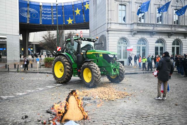 TOPSHOT - Farmers stand next to potatoes and a tractor parked in front of the European Parliament, during a farmers' protest to denounce the reforms of the Common Agricultural Policy (CAP) and trade agreements such as the Mercosur, in Brussels, on December 18, 2025, organised by Copa-Cogeca, the main association representing farmers and agricultural cooperatives in the EU. EU Farmers, particularly in France, worry the Mercosur deal -- which will be discussed at the EU leaders meeting -- will see them undercut by a flow of cheaper goods from agricultural giant Brazil and its neighbours. They also oppose plans put forward by the European Commission to overhaul the 27-nation bloc's huge farming subsidies, fearing less money will flow their way. (Photo by NICOLAS TUCAT / AFP)