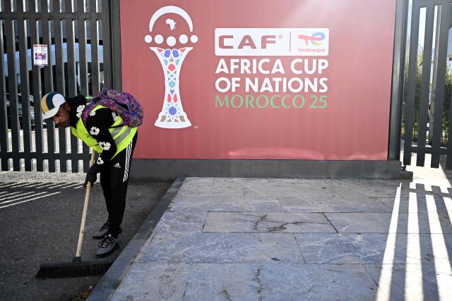 An employee sweeps the area close to the games' logo, as the final touches take place outside of the Al-Medina Stadium in Rabat, on December 18, 2025, ahead of the Africa Cup of Nations (AFCON). The competition begins on December 21. (Photo by Paul ELLIS / AFP)