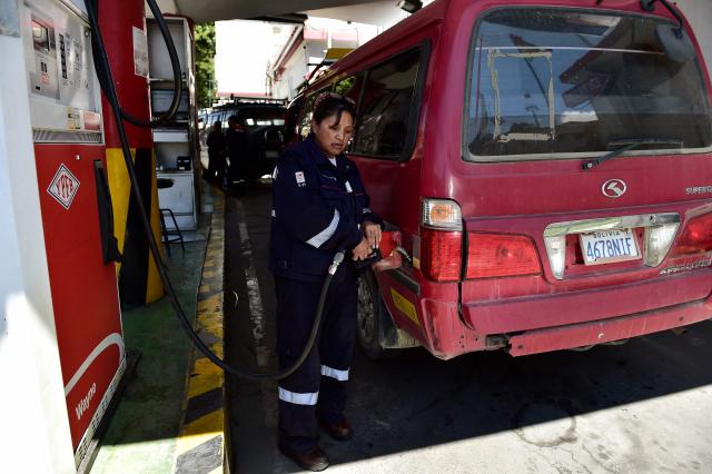 A worker loads fuel on a passengers van in La Paz on December 18, 2025. Bolivia's President Rodrigo Paz announced on December 17, 2025, the country will get rid of its fuel subsidies, ending 20 years of fixed prices under the Latin American nation's previous leftist leaders. (Photo by Jorge BERNAL / AFP)