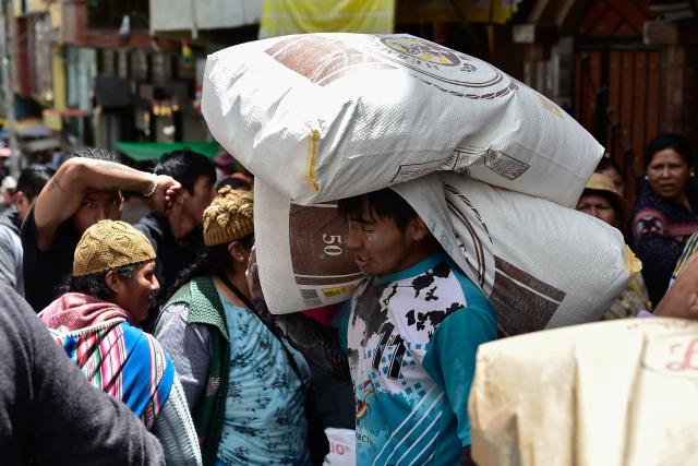 A worker carries sacks of food at a local market in La Paz on December 18, 2025. Bolivia's President Rodrigo Paz announced on December 17, 2025, the country will get rid of its fuel subsidies, ending 20 years of fixed prices under the Latin American nation's previous leftist leaders. (Photo by Jorge BERNAL / AFP)
