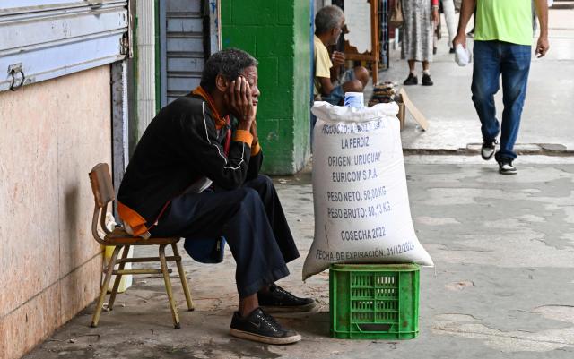 A man on a chair sells rice on a street in Havana on December 18, 2025. (Photo by YAMIL LAGE / AFP)