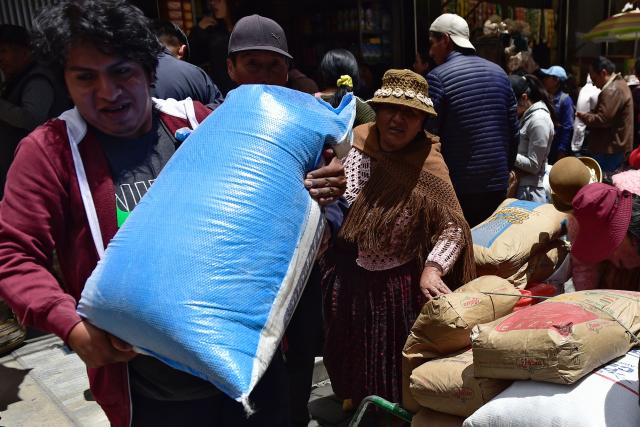 A worker carries a sack of food at a local market in La Paz on December 18, 2025. Bolivia's President Rodrigo Paz announced on December 17, 2025, the country will get rid of its fuel subsidies, ending 20 years of fixed prices under the Latin American nation's previous leftist leaders. (Photo by Jorge BERNAL / AFP)