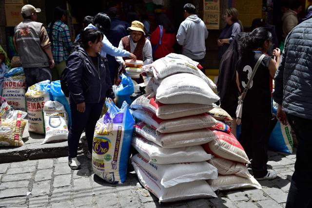 A woman stands next to sacks of food at a local market in La Paz on December 18, 2025. Bolivia's President Rodrigo Paz announced on December 17, 2025, the country will get rid of its fuel subsidies, ending 20 years of fixed prices under the Latin American nation's previous leftist leaders. (Photo by Jorge BERNAL / AFP)