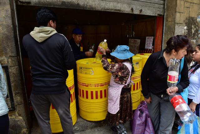 A Bolivian woman buys cooking oil at a local market in La Paz on December 18, 2025. Bolivia's President Rodrigo Paz announced on December 17, 2025, the country will get rid of its fuel subsidies, ending 20 years of fixed prices under the Latin American nation's previous leftist leaders. (Photo by Jorge BERNAL / AFP)