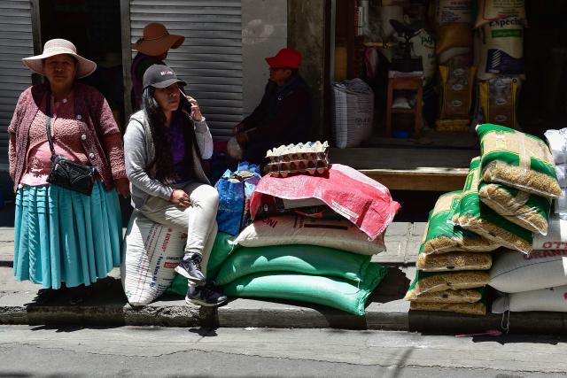 A Bolivian women uses her mobile phone next to groceries at a local market in La Paz on December 18, 2025. Bolivia's President Rodrigo Paz announced on December 17, 2025, the country will get rid of its fuel subsidies, ending 20 years of fixed prices under the Latin American nation's previous leftist leaders. (Photo by Jorge BERNAL / AFP)