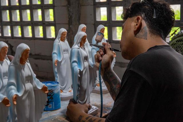A worker sprays paint onto Christian religious statues at the Studio Malta Jaya handicraft workshop in Bantul, Yogyakarta, on December 18, 2025, ahead of Christmas celebrations. (Photo by DEVI RAHMAN / AFP)